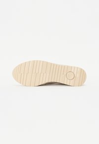 Suola delle scarpe beige, caratterizzata da una superficie in gomma testurizzata con scanalature orizzontali e un logo circolare. Design piatto e largo per stabilità.