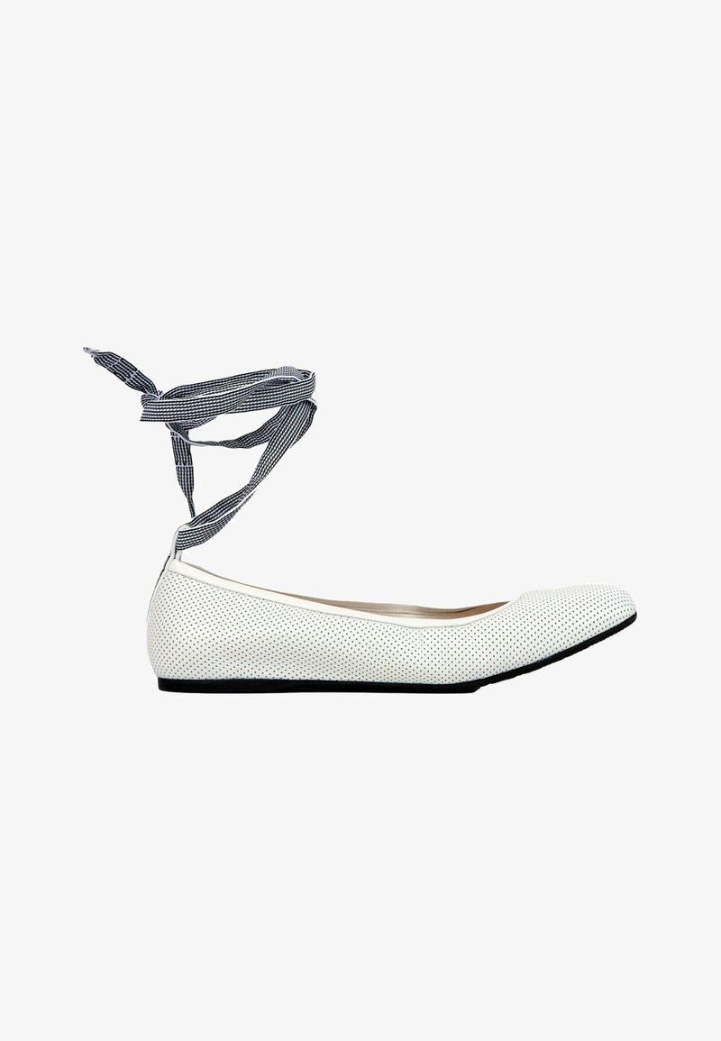 Chaussure de ballet plate blanche perforée avec semelle noire et rubans à nouer rayés noir et blanc à la cheville.