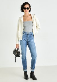 Lys beige zip-up hettegenser, grå stroppeløs topp, slitt lyseblå jeans og svarte platåstøvler. Tilbehør: liten svart håndveske.