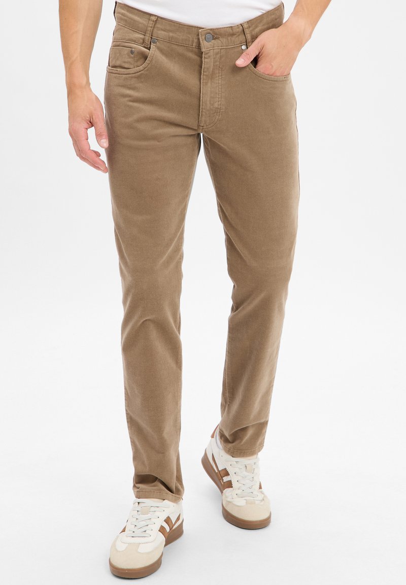 Brown, soft cotton blend pants with a straight leg, five-pocket design, and metal buttons. Paired with white sneakers featuring brown accents.