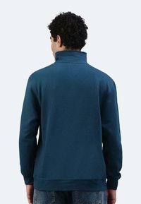 Dunkelblauer Pullover mit hohem Kragen, langen Ärmeln und gerippten Bündchen. Weiches Material mit glatter Textur, das eine subtile Nahtdetail auf der Rückseite aufweist.