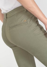 Olijfgroene broeken met een slim fit, voorzien van een achterzak en subtiele logo-details. De stof is glad met een lichte glans.