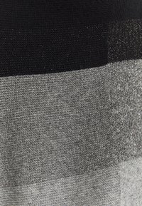 Stickad tyg i svart och grå nyanser, med horisontella ränder. Texturen verkar mjuk med en lätt lyster i vissa områden.