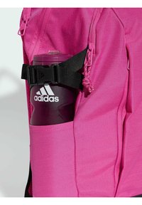 Lyserød sportsrygsæk med en sidelomme, hvor der er en sort rem, der holder en mørk lilla vandflaske med et hvidt Adidas-logo.