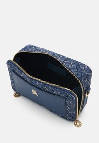 Niebieska skórzana torba z wzorzystą tkaniną i suwakiem, z logo w odcieniu złota oraz okrągłymi akcentami metalowymi, częściowo otwarta, ukazując wnętrze.