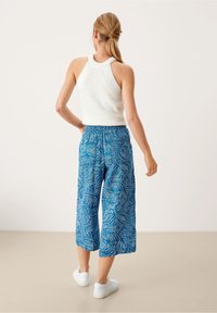 Valkoinen ribbineuloksinen toppi, jossa on korkea pääntie, yhdistetty sinisiin kuvioituihin leveälahkeisiin lyhytlahkeisiin housuihin, joissa on lehtikuvioita ja joustava vyötärö.