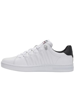 Zapatilla blanca de corte bajo con lengüeta trasera negra, cierre de cordones, detalles de costura lateral y suela de goma, mostrada desde el lado exterior.