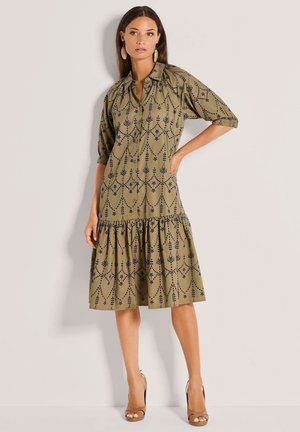 Olijfgroene jurk met een knoopsluiting aan de voorkant, driekwart mouwen en een gelaagde rok; heeft marineblauwe bloemenpatronen en een losse pasvorm.