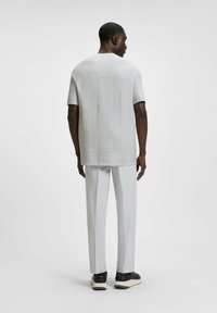Light gray short-sleeve shirt with a textured pattern, paired with straight white trousers and black sneakers with a cream sole.