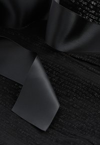 Black fabric with a textured surface featuring small sequins, paired with smooth black satin ribbons draped across the material.