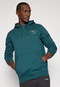 Sudadera azul verdosa de mezcla de algodón, con un bolsillo canguro, cordón ajustable y logo bordado que dice "PUMA ATHLETICS fundado en 1948".