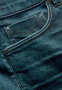 Țesătură de denim de culoare teal închis, cu o buzunar frontal, cusături contrastante și accente metalice. Textura pare moale, cu un ușor luciu.