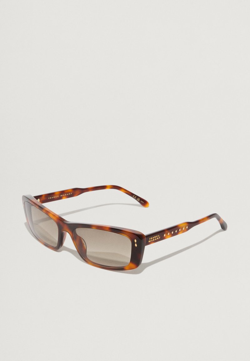 Occhiali da sole con montatura in plastica tartarugata, lenti squadrate e lenti color marrone. Accentuati da piccoli bottoni metallici sulla tempia.