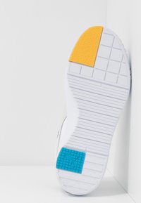 Semelle de basket blanche avec une section texturée jaune sur l'orteil et une section bleue avec le logo Puma sur le talon, sur fond blanc.