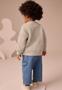 Pull gris clair en maille avec poignets côtelés, associé à un pantalon cargo en denim bleu ample avec poches latérales et des baskets beiges.