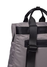 Mochila de tela gris con correas y detalles en negro, que cuenta con un bolsillo con cremallera y un detalle de logo. Material texturizado con un diseño duradero.