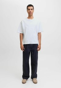 Tricou oversized gri deschis dintr-un material moale, asociat cu pantaloni evazați de culoare bleumarin închis. Încălțăminte bej cu cusături și șireturi vizibile.