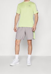 Jasnozielona koszulka sportowa z szarymi akcentami, sparowana z szarymi szortami. Obuwie to białe trampki. Minimalistyczny design z funkcjonalnym stylem.