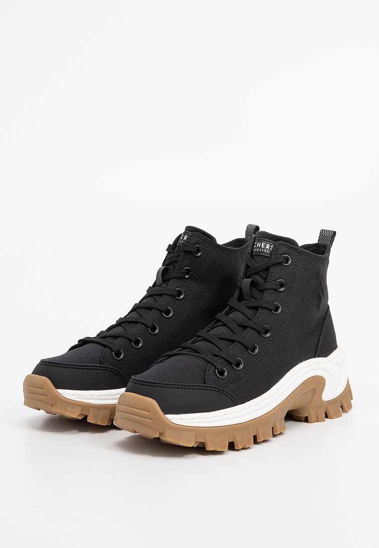 Schwarze High-Top-Sneaker mit dicken weißen Zwischensohlen und klobigen braunen Gummisohlen, ausgestattet mit schwarzen Schnüren und Stoff-Schlaufen an der Ferse.