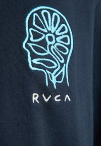 Blau besticktes abstraktes Gehirndesign mit Blumenmustern auf dunklem Stoff über dem weiß bestickten Text „RVCA“.