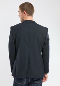 Blazer bleu marine foncé, coupe ajustée, tissu lisse avec épaules structurées, fente arrière unique, et boutons accent argentés sur les manches.