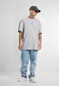 Gray oversized t-shirt with blue embroidery, paired with light blue distressed denim jeans featuring rips and white sneakers.