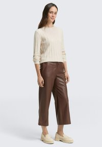 Strickpullover in Creme mit geripptem Muster, kombiniert mit braunen, cropped Hosen aus Kunstleder und beigen Plateauschnürern. Einfaches, modernes Design.