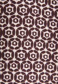 Tissu en coton avec un motif géométrique aux couleurs marron et crème, composé de formes hexagonales entourées d'accents en forme de feuilles.