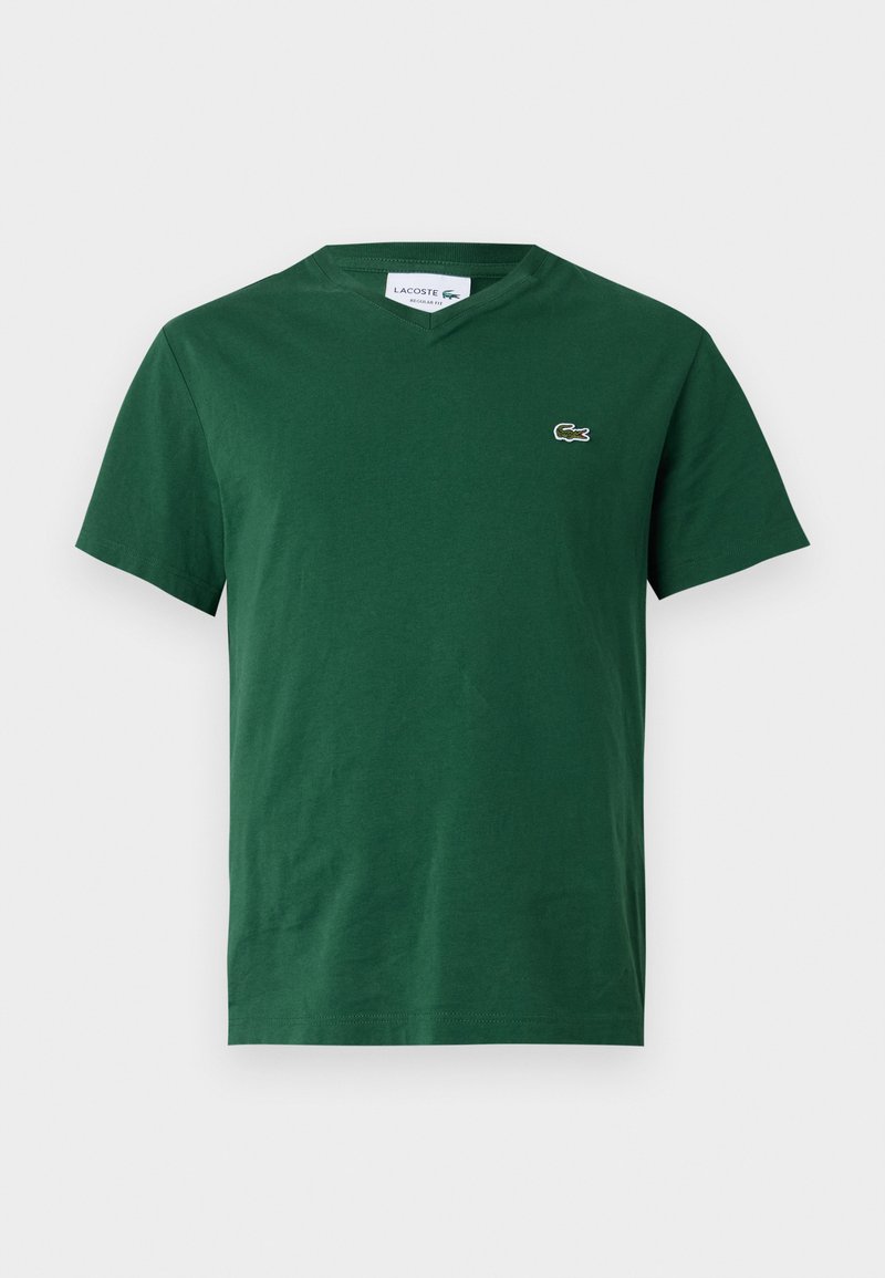 T-shirt en coton vert avec col en V, manches courtes et un petit logo brodé sur la poitrine gauche. Texture lisse, coupe décontractée.