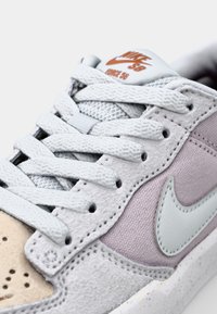 Nike SB Force 58 športni čevelj z zgornjim delom iz svetlo sivega semiša, vijoličnimi tekstilnimi detajli, sivimi vezalkami in belo podplatom z luknjami.