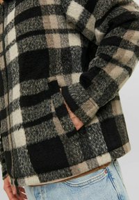 Giacca in pile a quadri con un mix di nero, bianco e grigio; tasche foderate; e una vestibilità comoda con zip davanti.