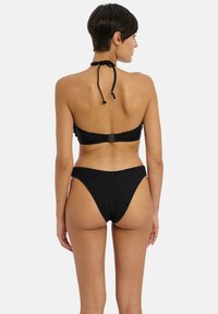 Černý bikiny set s halter topem, který má nastavitelné zavazování za krkem, strukturovanou látku a vysoké kalhotky. Viditelné zapínání na zádech.