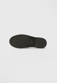 Semelle de chaussure noire avec une texture lisse et un motif de semelle subtil. Présente un bord net et une empreinte de logo, indiquant la taille et la marque.