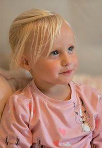 Child wearing a light pink long-sleeve shirt with cartoon animal prints and hearts. Soft fabric, round neck, and short puffy sleeves.