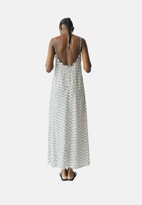 Ärmelloses Maxikleid in Weiß mit einem schwarz-geometrischen Muster, mit einem tiefen Rückenausschnitt und geradem Schnitt, kombiniert mit schwarzen Sandalen.