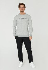 Sudadera gris con mangas largas, cuello redondo y gráfico negro de "SAIL RACING". Combinada con pantalones negros y zapatillas blancas.