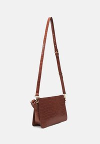 Sac à bandoulière en simili-cuir crocodile marron avec une bandoulière ajustable et des accents en métal doré. Il présente une forme rectangulaire et une finition texturée.