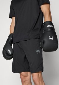 Gants de boxe noirs avec des accents blancs, associés à un t-shirt noir à manches courtes et un short noir arborant un design de logo subtil.