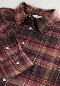 Red and beige plaid flannel shirt with a button-down collar and white buttons. Features a soft texture and a standard fit.