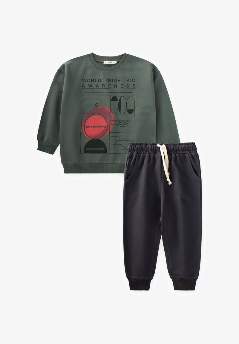 Green sweatshirt with graphic print and text; paired with dark gray elastic-waist joggers featuring side pockets. Soft, casual materials.