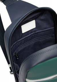 Interno di uno zaino blu navy con finitura testurizzata, dotato di una tasca con zip e un'etichetta bianca su una fodera in tessuto scuro.