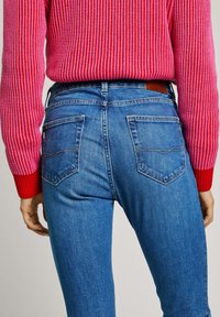 Modré džíny s přiléhavým střihem, se dvěma zadními kapsami, rovný střih a viditelné švy. Kombinováno s růžovým pleteným svetrem.