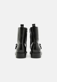 Botas de tobillo de cuero negro con un acabado brillante, cierre de cremallera, lengüetas de tirón y un tacón bajo apilado. Textura suave sin patrones visibles.