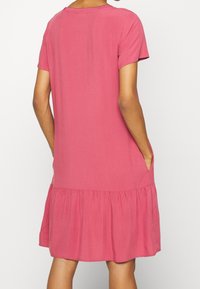 Kurzärmliges pinkes Kleid aus weichem Stoff, mit Rundhalsausschnitt, Rüsche am Saum und seitlichen Taschen.