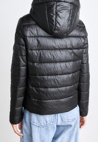 Czarna pikowana kurtka z kapturem, o gładkiej fakturze i elastycznym dole. Tył prezentuje smukły, dopasowany krój.