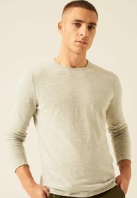 Lichtgrijs langemouwen T-shirt in een geribbelde textuur met een ronde hals. De stof lijkt zacht en lichtgewicht, met aansluitende mouwen.