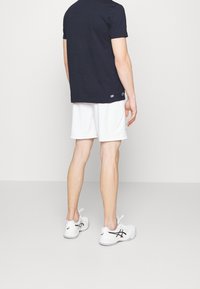 Marinblå T-shirt, vita shorts och vita sportskor med svarta accenter. T-shirten har en enkel design med rund halsringning och korta ärmar.