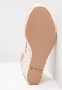 Vue unique d'une sandale compensée beige avec talon en espadrille tressée et semelle extérieure en caoutchouc lisse sur fond blanc.
