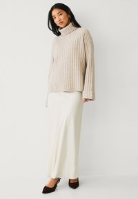 Cremfarbener, gerippter Rollkragenpullover mit langen Ärmeln, kombiniert mit einem glatten weißen Maxirock und dunkelbraunen Slingback-Heels.