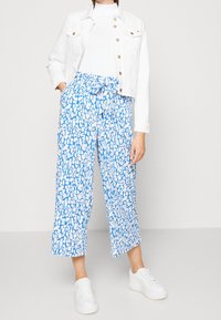 Blauw-witte wijde pijpen broek met een ceintuur in de taille, gecombineerd met een wit cropped jack en witte sneakers. Gladde stoftextuur.